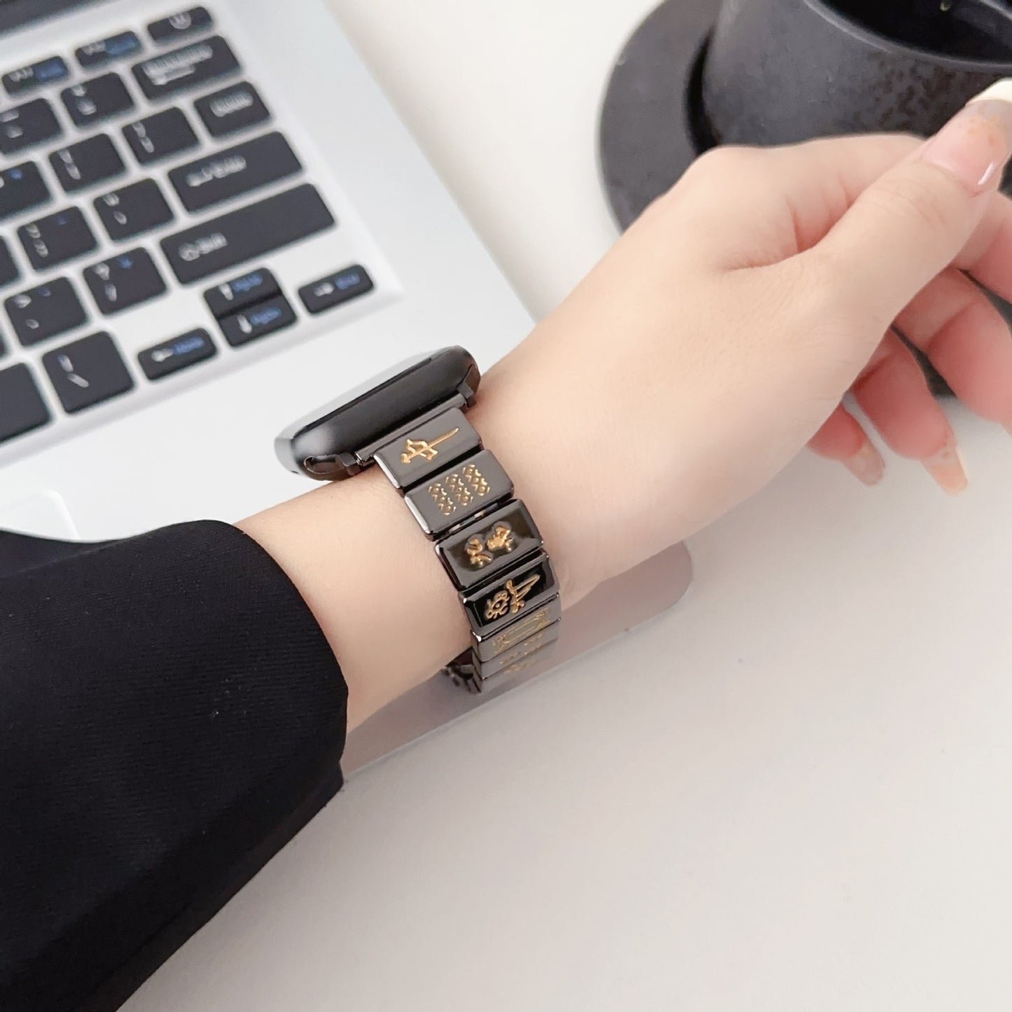 Mahjong-themed Apple Watch band in black and gold, featuring a hand wearing the band while using a laptop